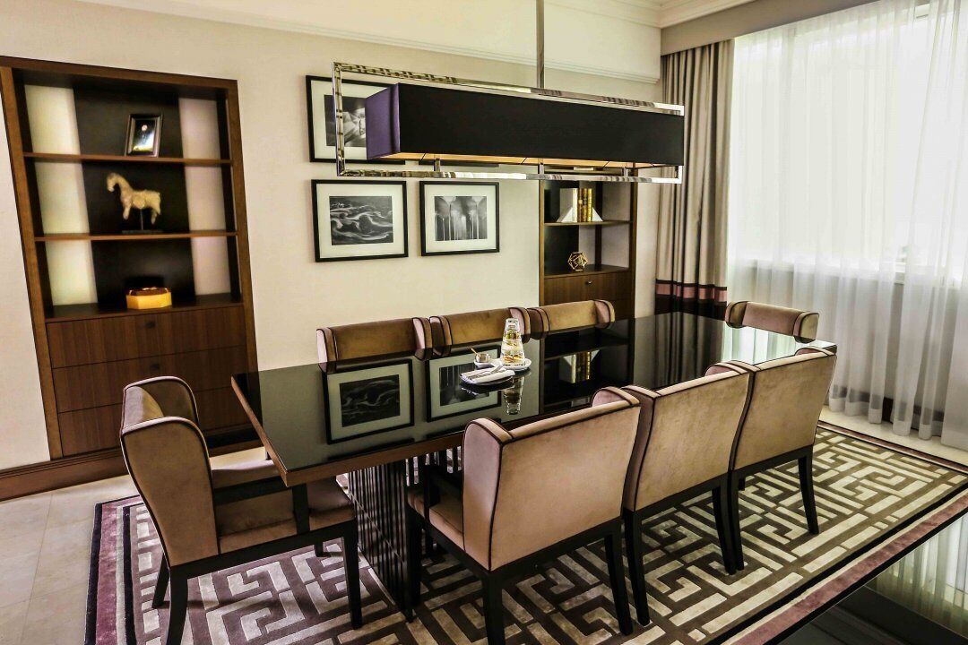 Un coin repas avec une table en verre, des chaises rembourrées, un tapis à motifs et une bibliothèque agrémentée de photos encadrées et d’objets décoratifs.