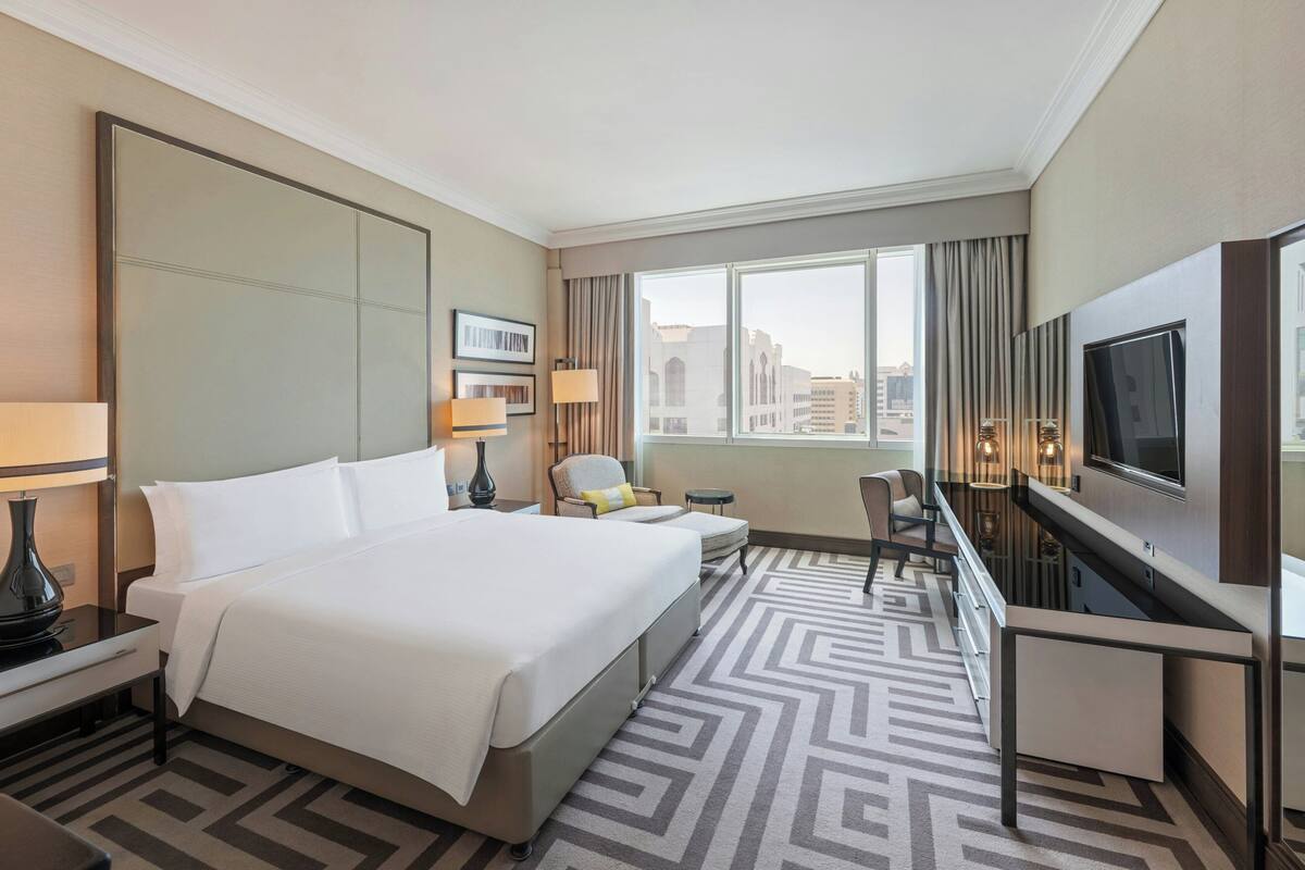 Een hotelkamer met een groot bed, een bureau, een televisie en uitzicht op de stad.