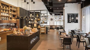 A modern cafe with a central counter, shelves with jars and bottles, and a menu board.