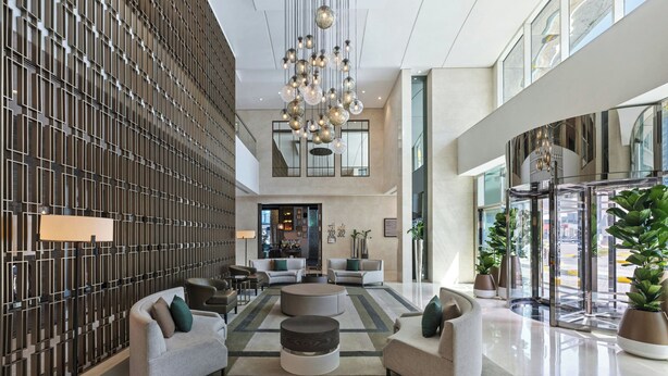 A modern lobby with a high ceiling, a large chandelier, and a seating area with sofas and a coffee table.