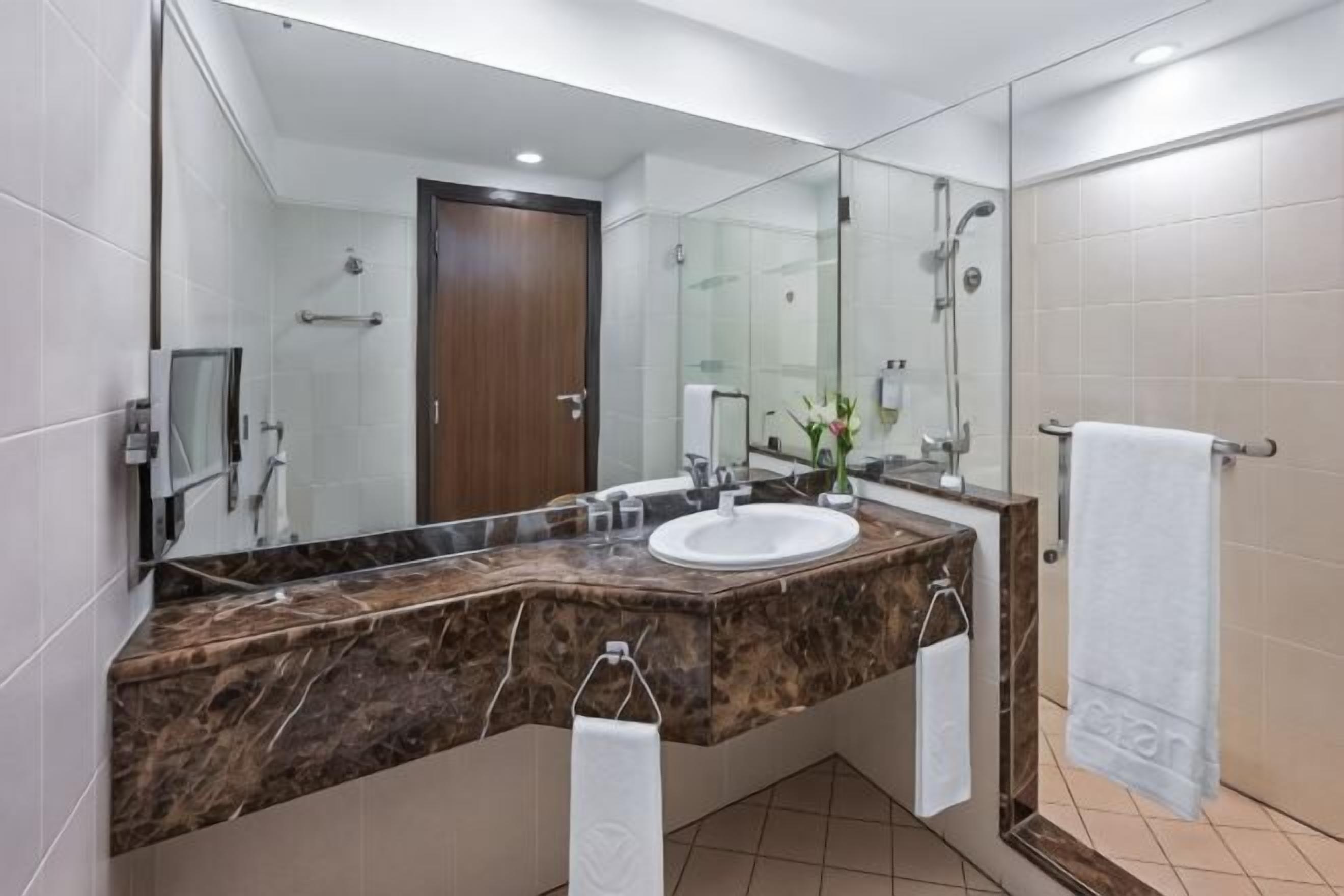 Un baño moderno con tocador de mármol, un espejo grande, un lavabo y una zona de ducha.