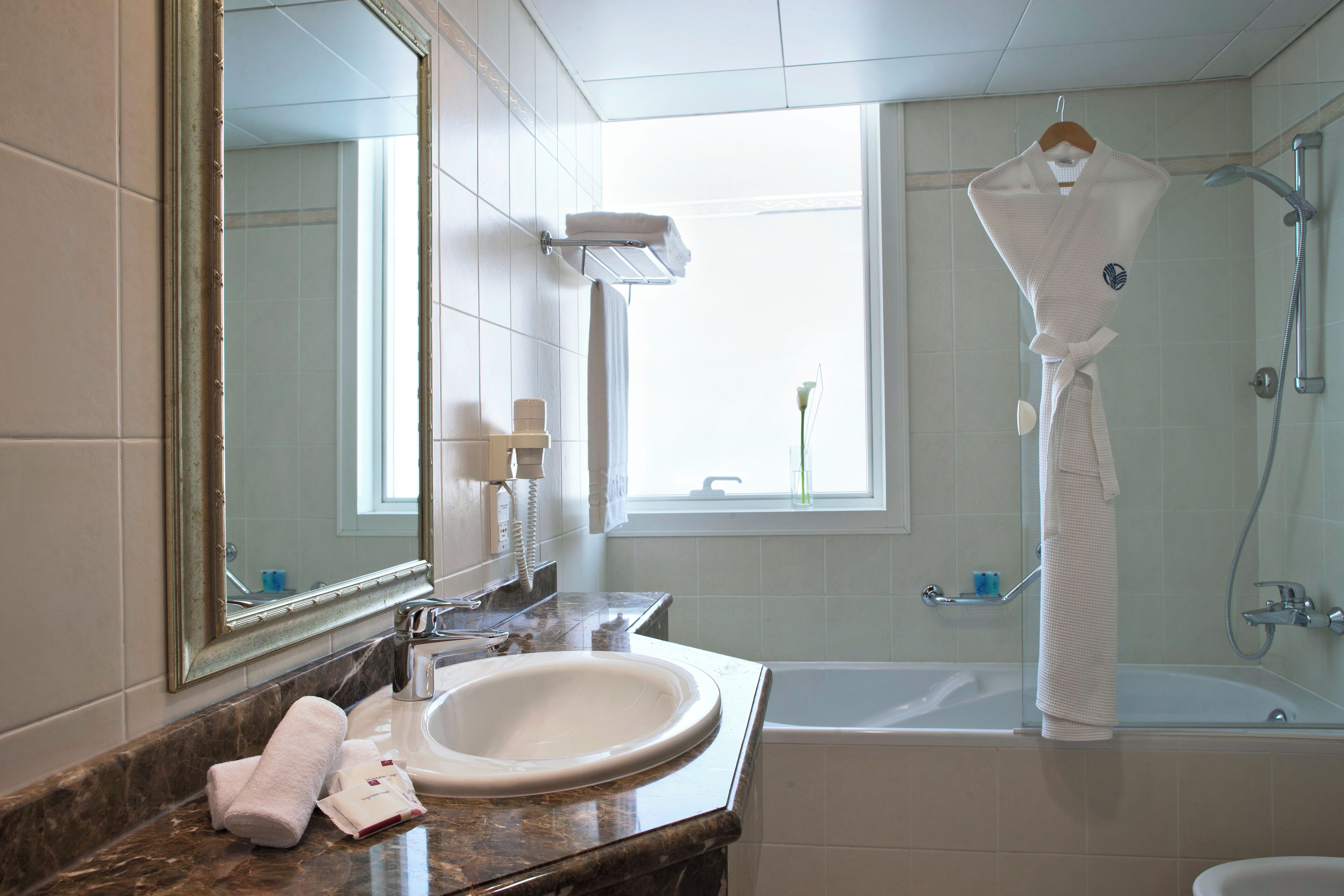 Ein Badezimmer mit Marmorwaschbecken, einem großen Spiegel, einer Badewanne und einem Bademantel, der auf einem Haken hängt.