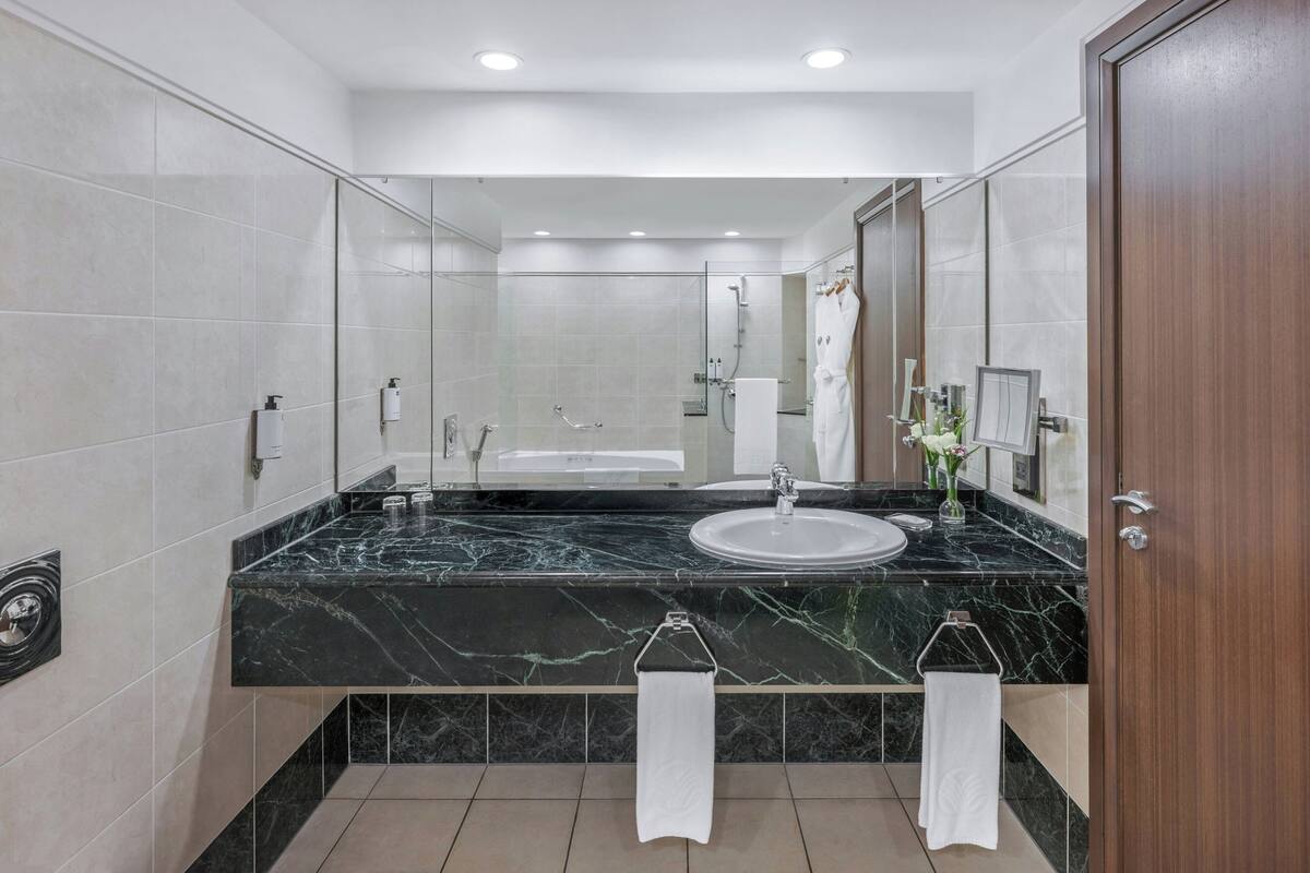 Een moderne badkamer met een zwarte marmeren wastafel, een witte wasbak, een douche met glazen wand en een houten deur.