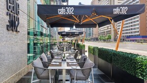 Terrasse avec tables et chaises, une enseigne indiquant « Café 302 », et une vue sur une rue de la ville en arrière-plan.