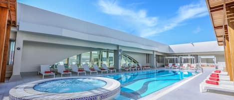 A modern outdoor pool area with lounge chairs and a hot tub.