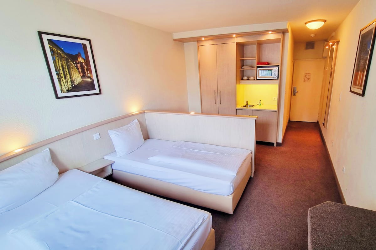 A hotel room with two beds, a kitchenette, and a hallway leading to another room.