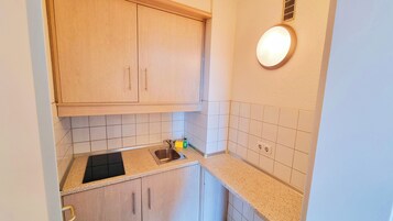 Eine kleine Küche mit Holzausstattung, einer schwarzen Arbeitsplatte und einer Wandleuchte.