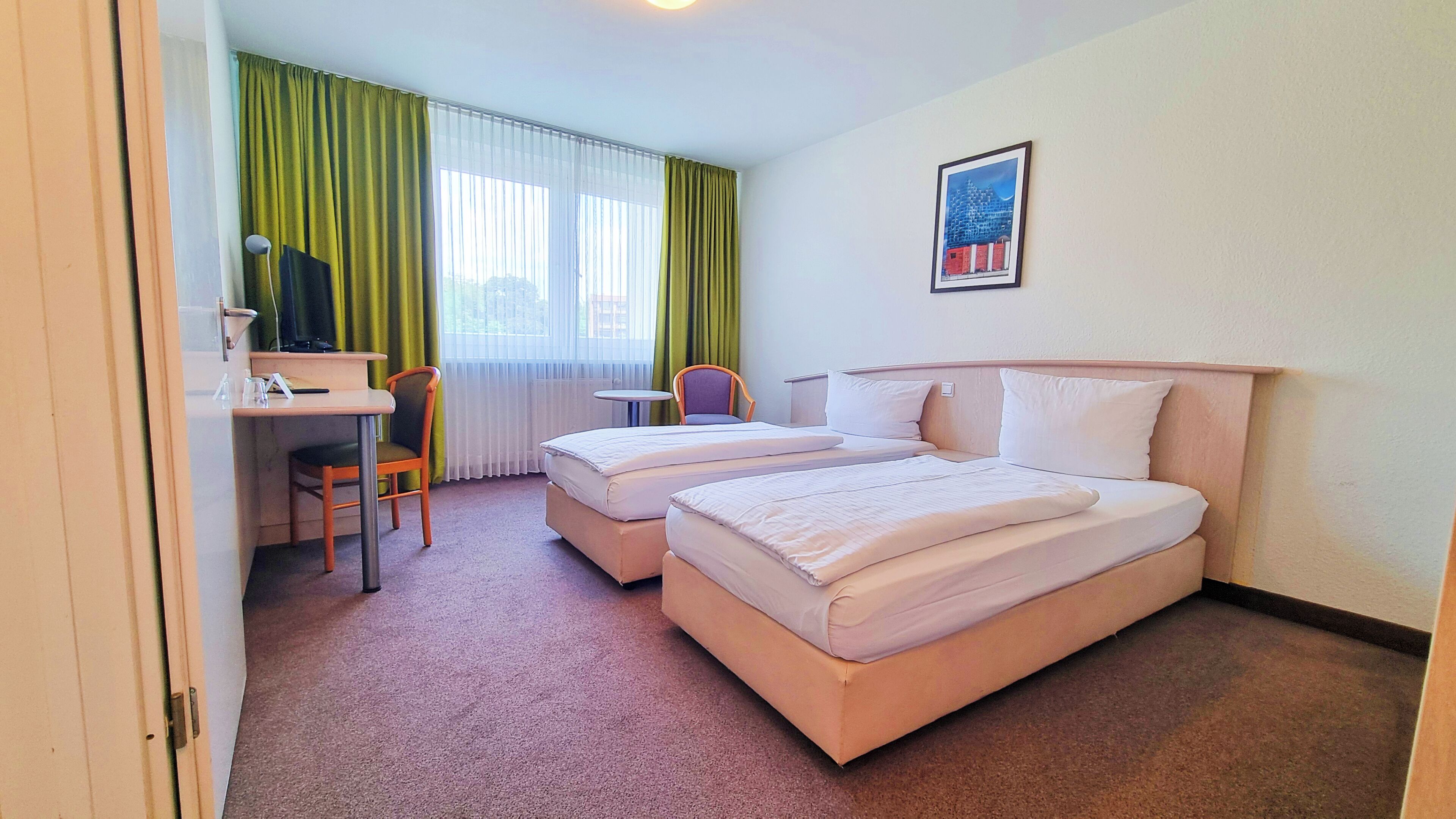 A hotel room with two beds, a desk, a chair, and a window with curtains.