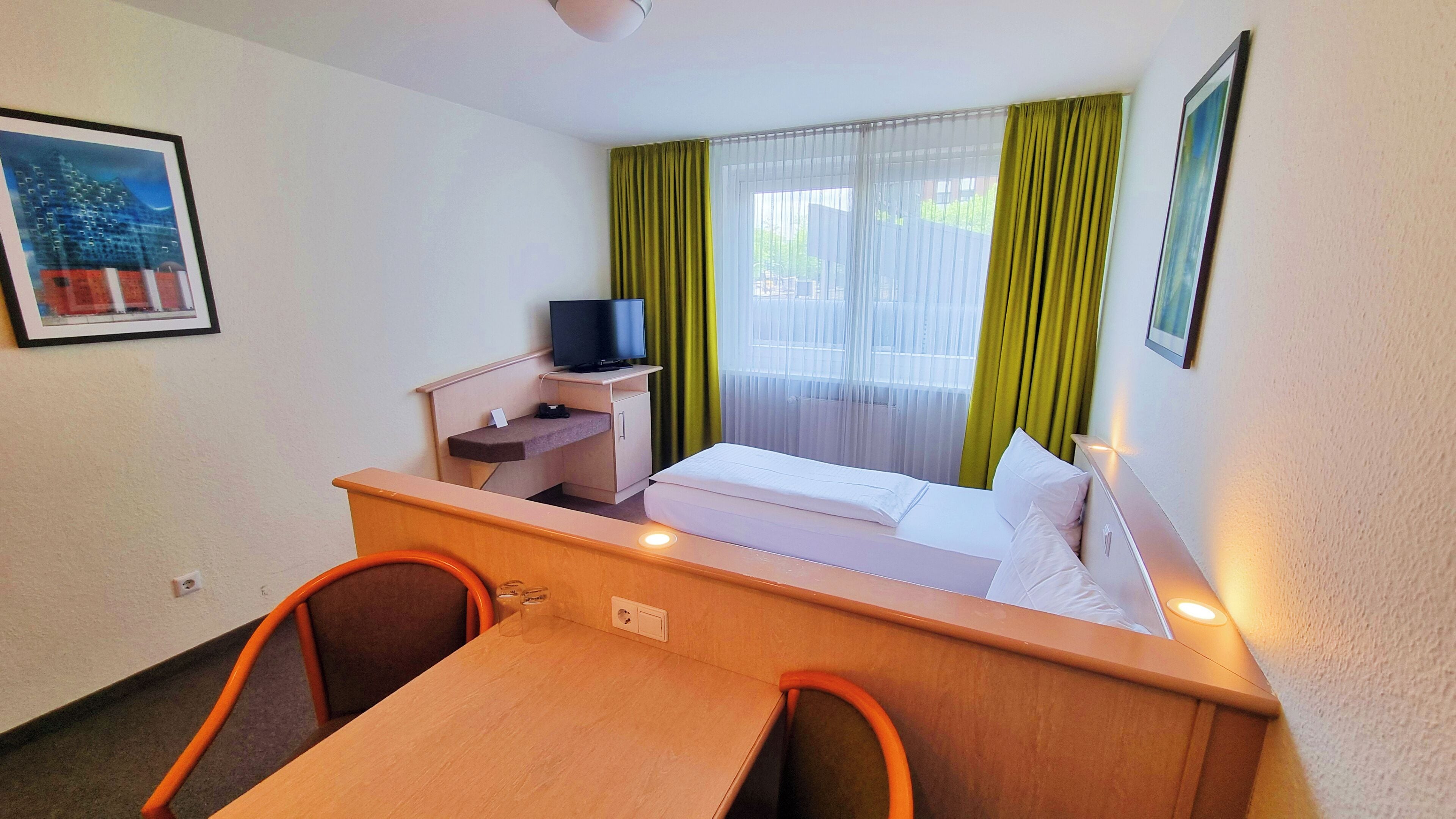 A hotel room with a bed, a desk with a television, a small table, and two chairs.