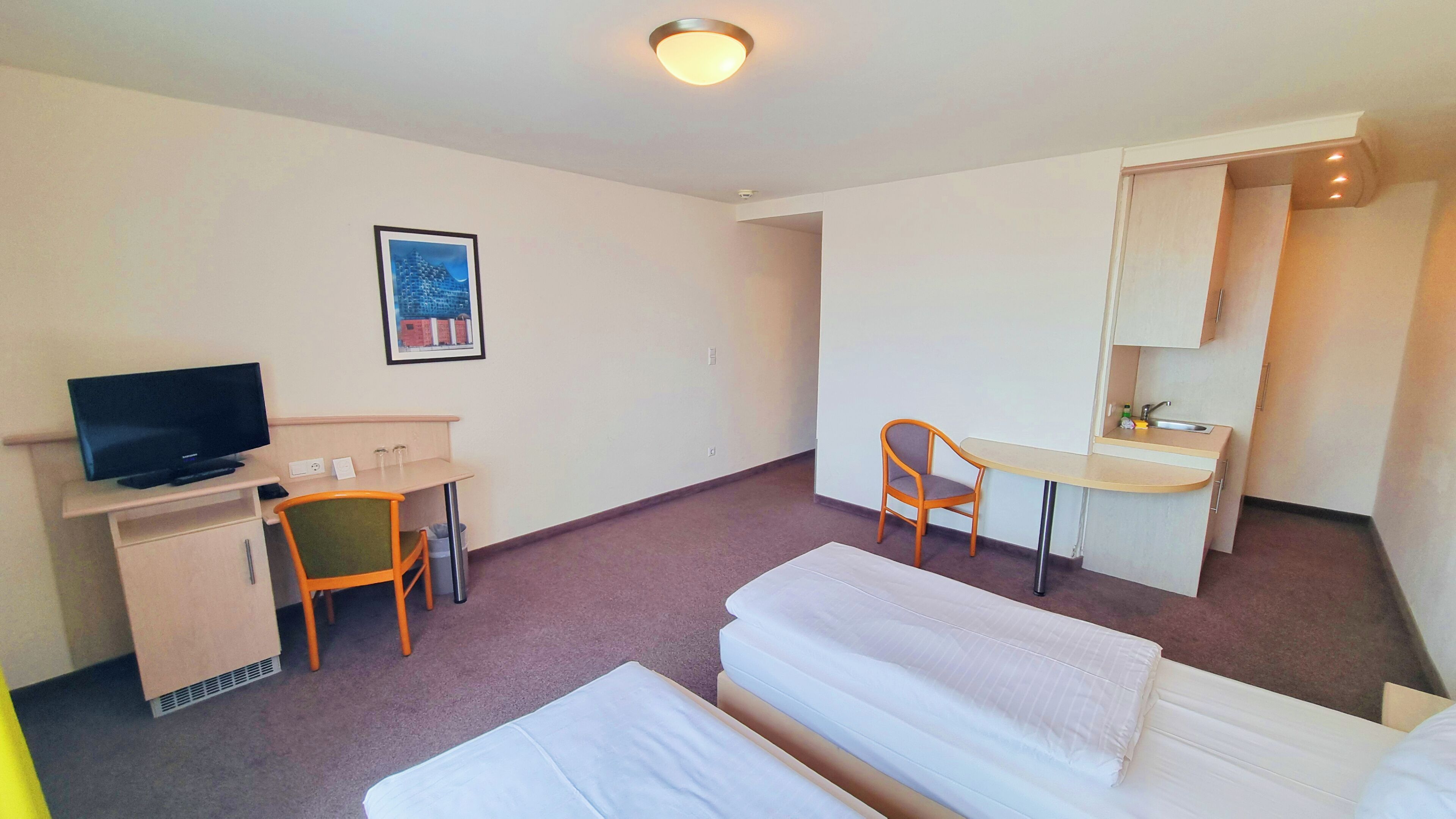 A hotel room with a bed, a desk with a chair, a television, and a framed picture on the wall.