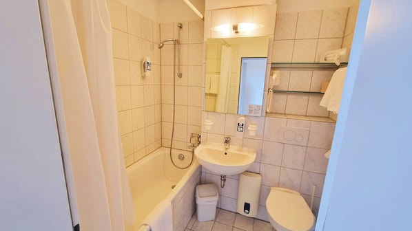 A bathroom with a bathtub, sink, toilet, and a shower with grab bars.