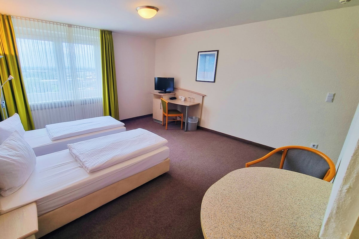 A hotel room with two beds, a desk with a computer, a chair, and a small table.