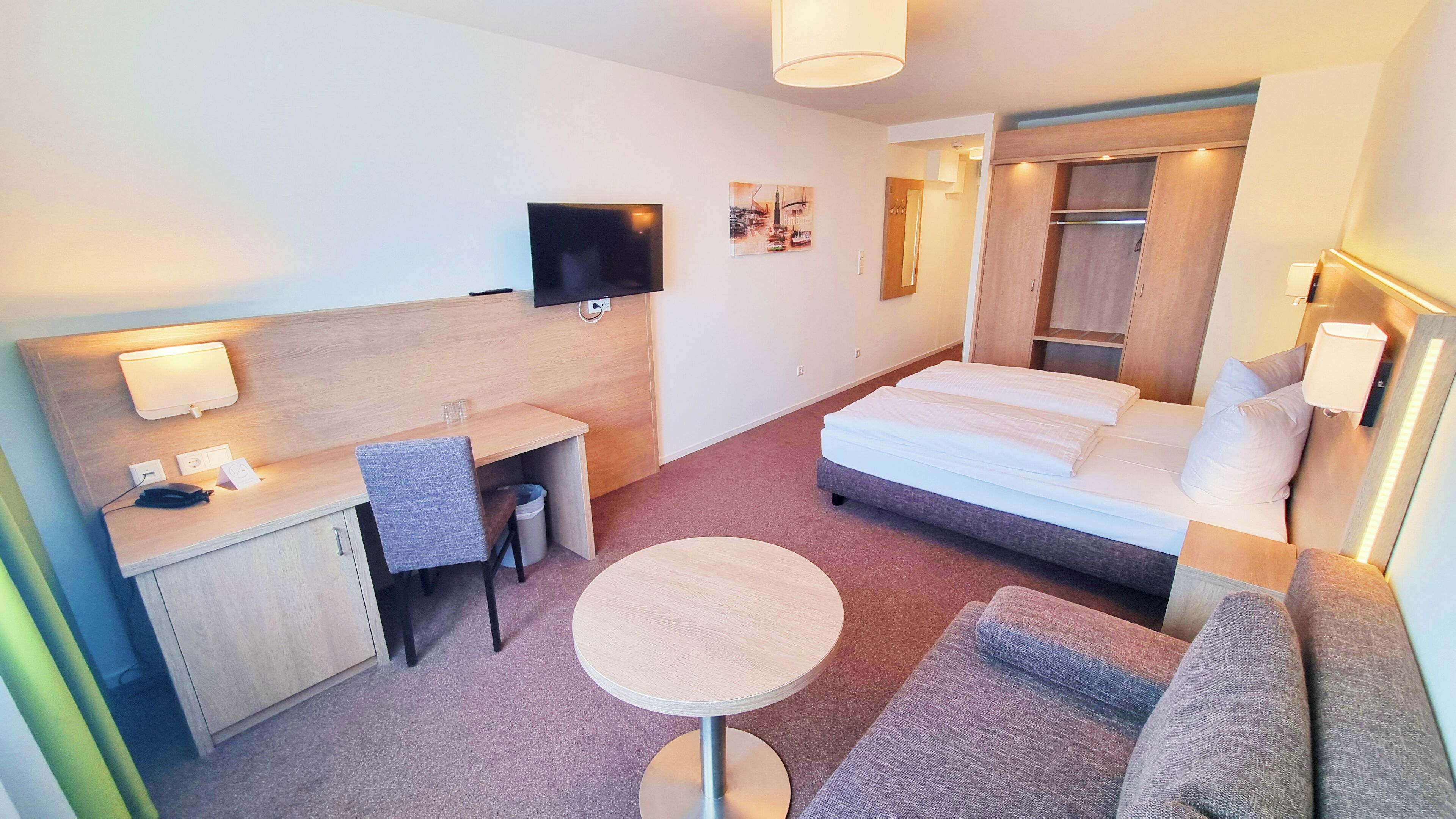 Une chambre d’hôtel avec un lit, un bureau, une chaise, une table ronde et un téléviseur.