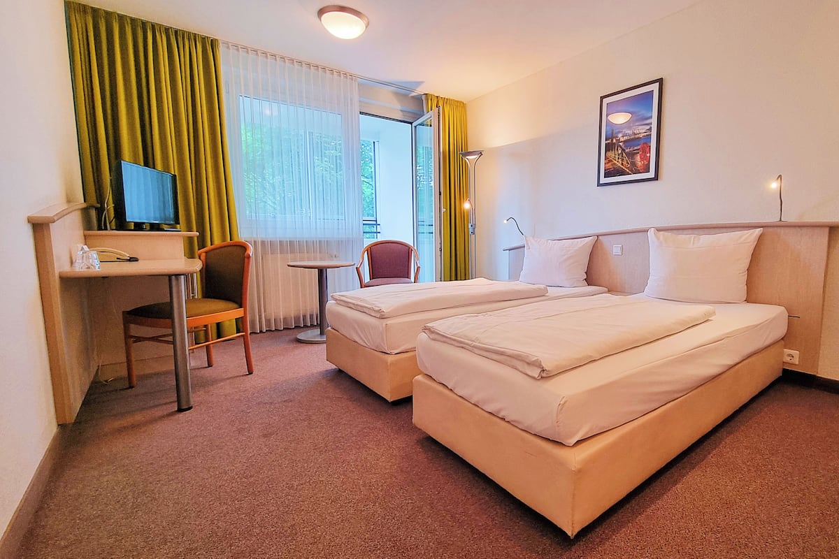 A hotel room with two beds, a desk, a chair, and a window with curtains.