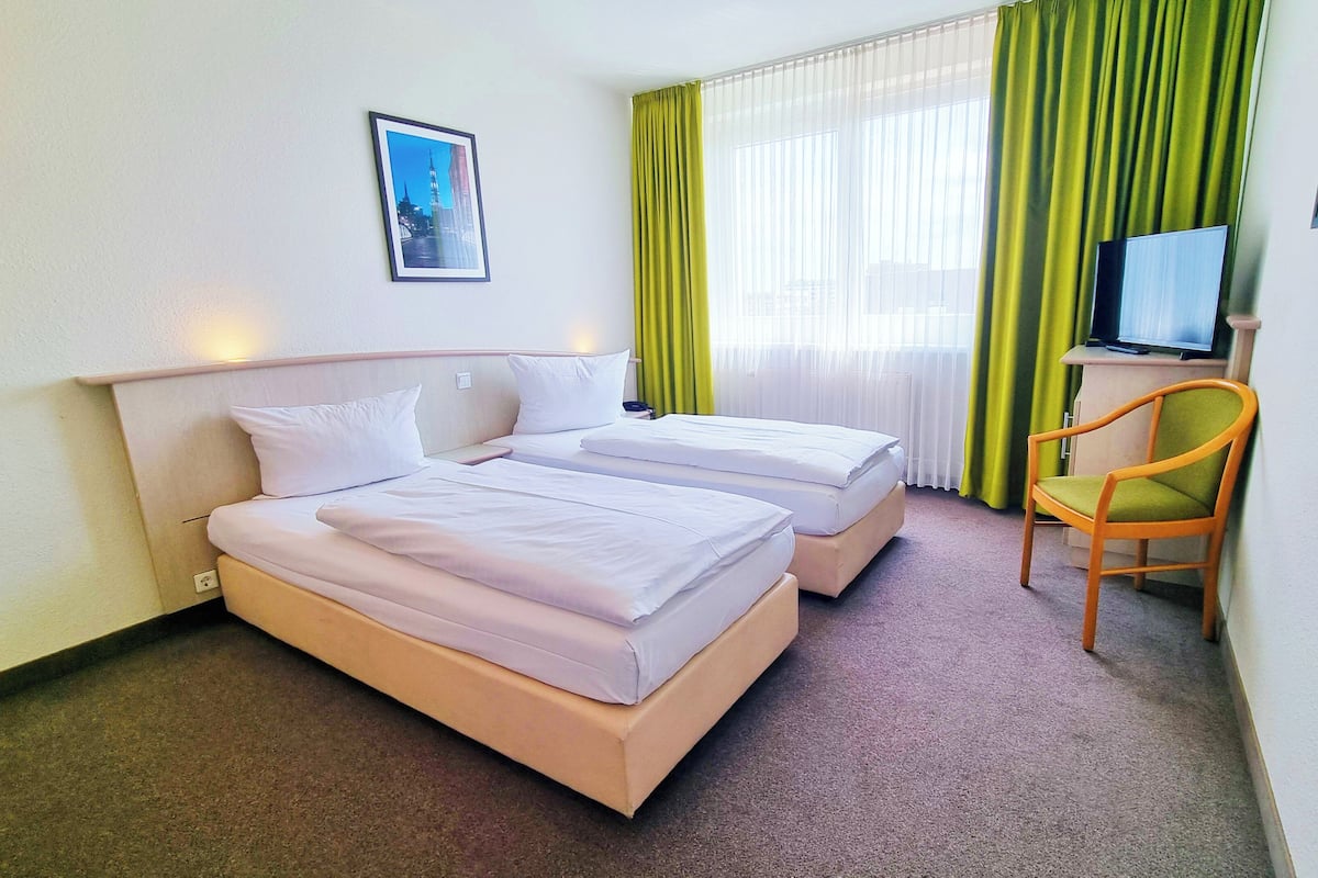 A hotel room with two beds, a desk, a chair, a television, and a framed picture on the wall.