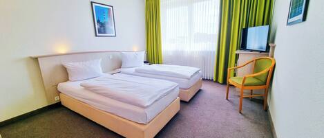 A hotel room with two beds, a desk, a chair, a television, and a framed picture on the wall.