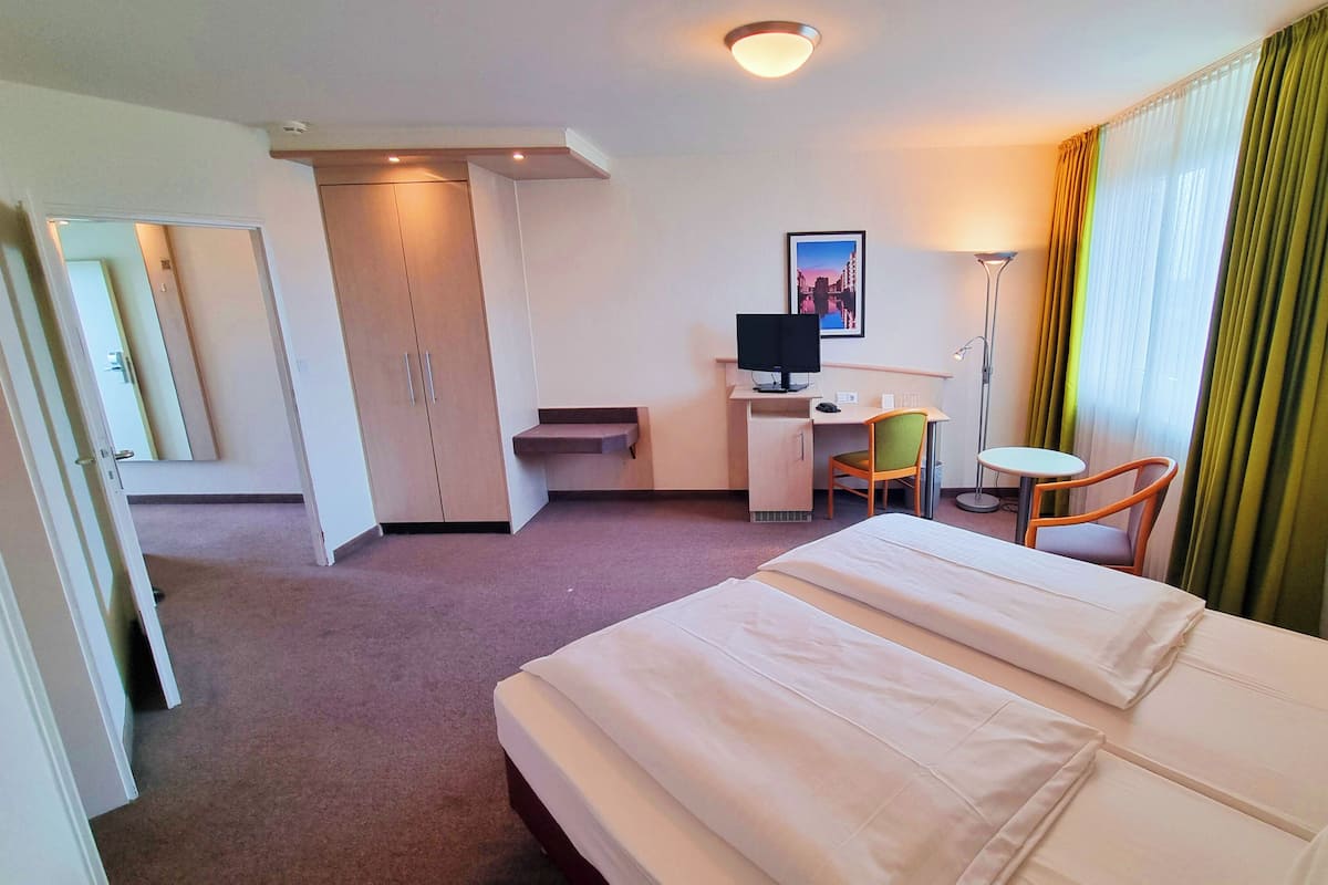A hotel room with a bed, a desk with a computer, a chair, and a television.