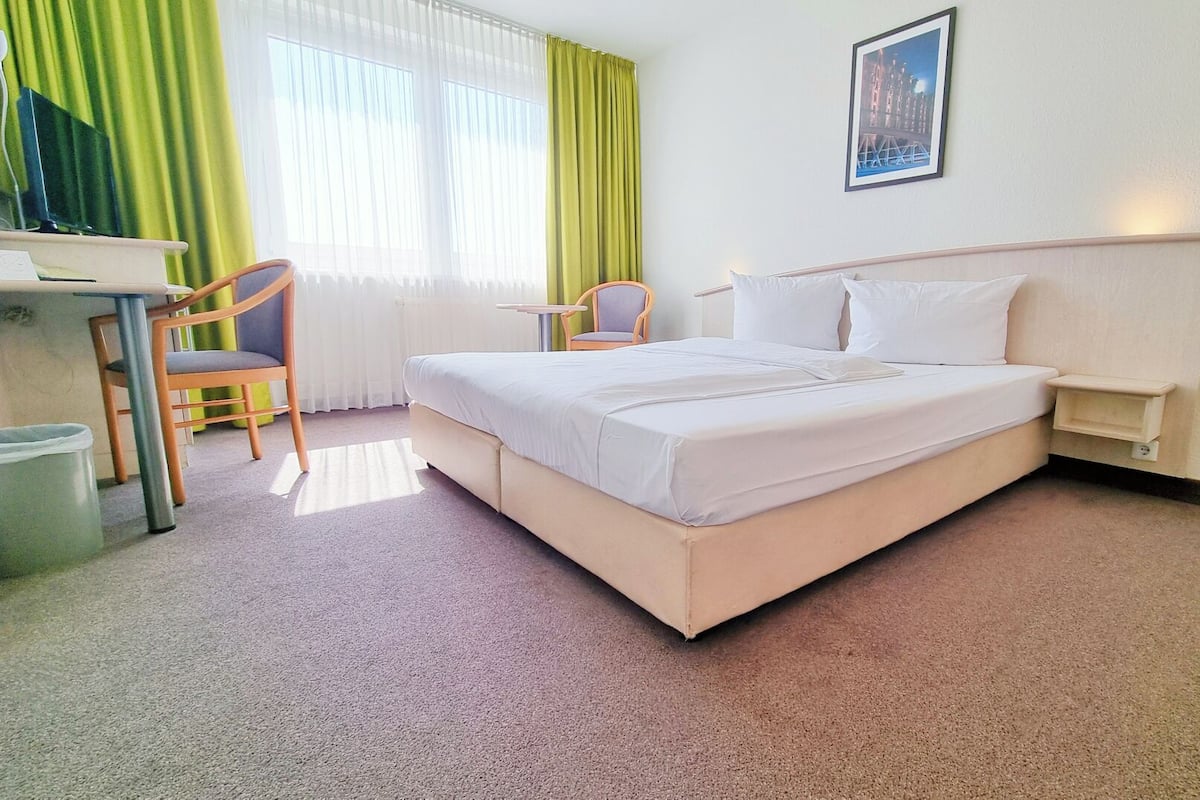 A hotel room with a bed, a desk, a chair, and a picture on the wall.