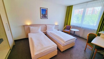 Ein Hotelzimmer mit zwei Einzelbetten, einem kleinen Tisch, einem Stuhl und einem Bild an der Wand.
