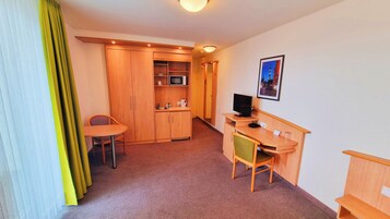 Ein kompaktes Hotelzimmer mit Küchenzeile, einem Einzelbett, einem Schreibtisch mit Stuhl und einem Fernseher.