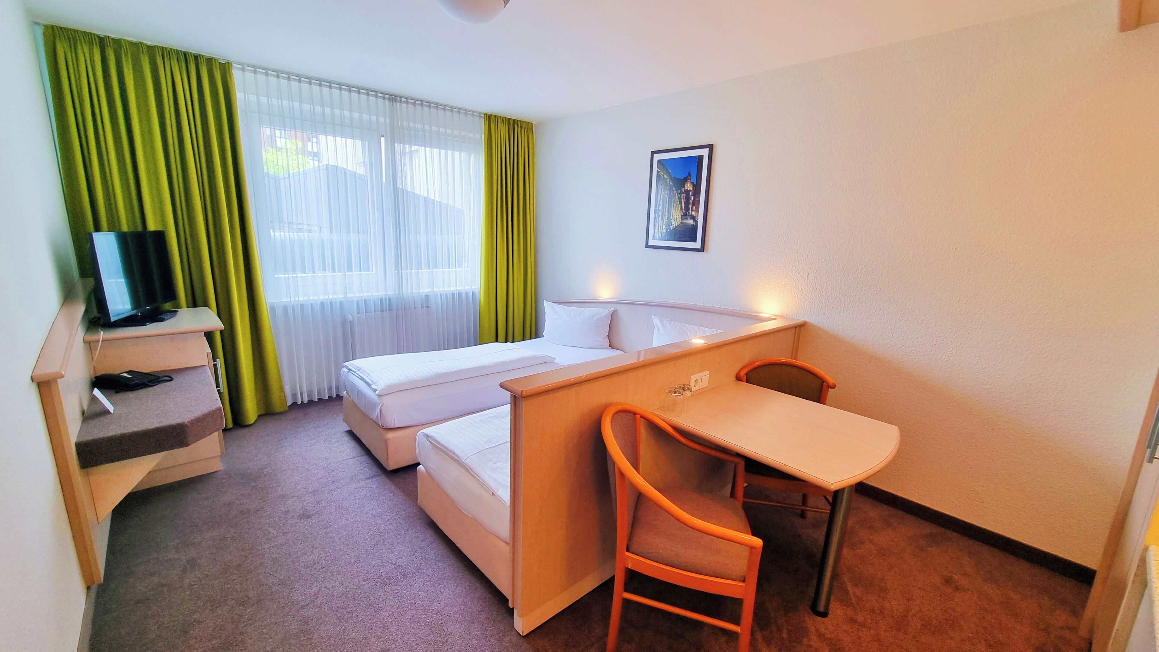 A hotel room with a bed, a desk, a chair, a television, and a picture on the wall.