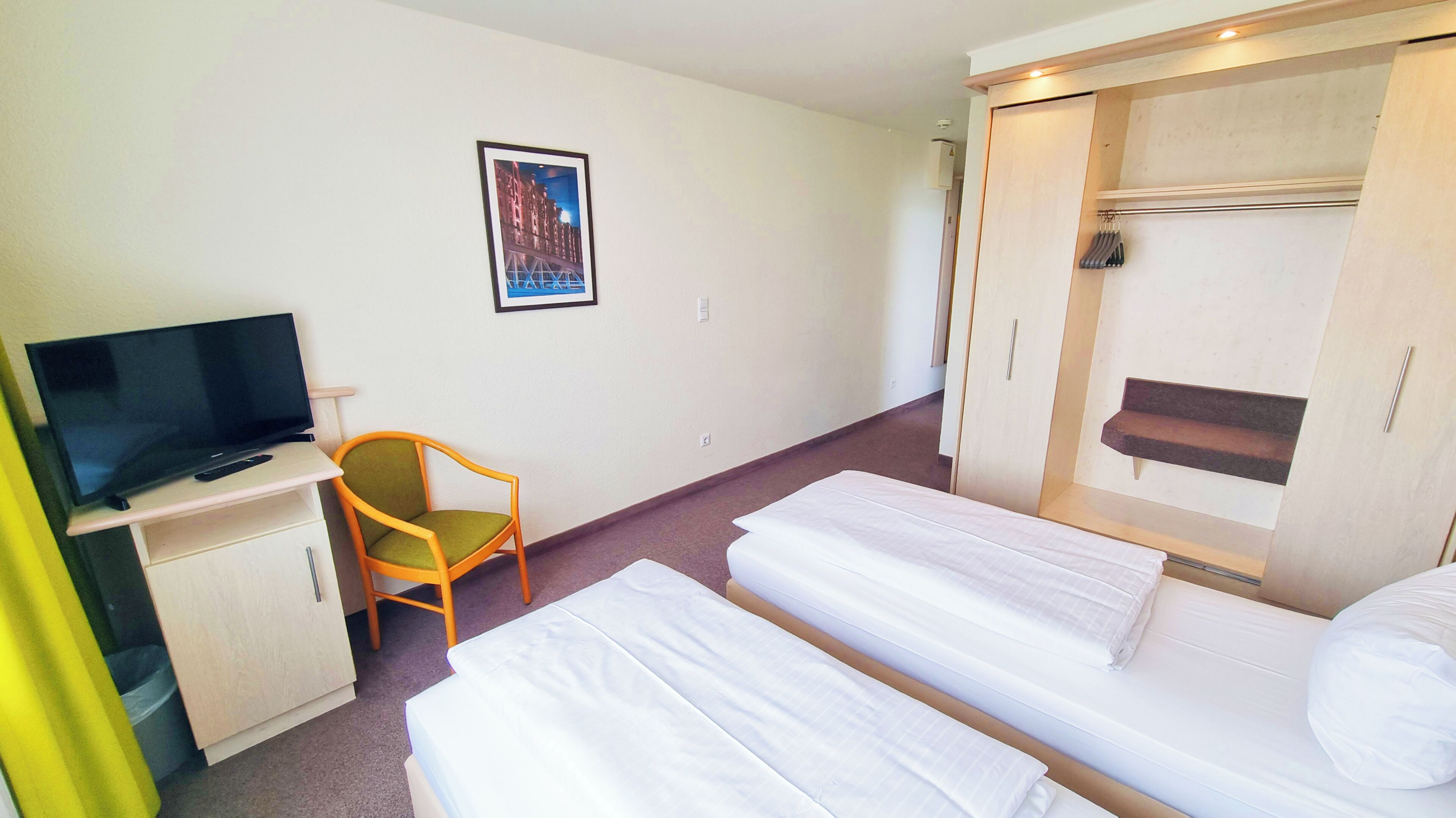 A hotel room with a TV, a chair, two beds, and a wardrobe.