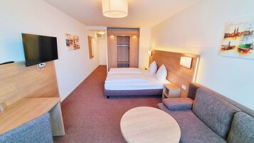 Una habitación de hotel con cama, televisión, sofá y una mesa redonda.