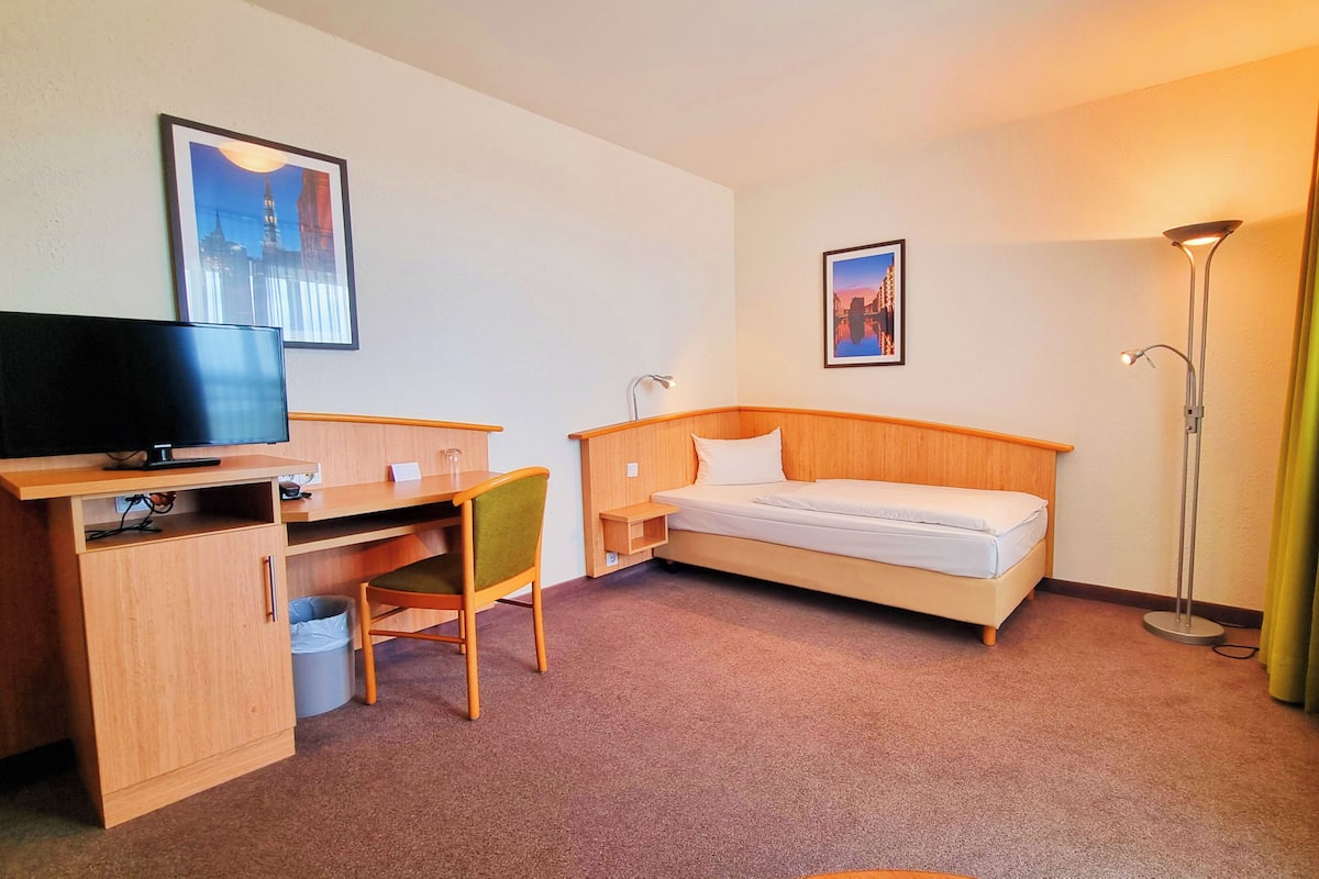 A hotel room with a bed, desk, chair, TV, and two framed pictures on the wall.