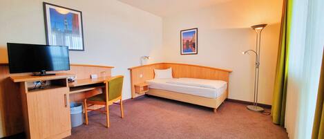 A hotel room with a bed, desk, chair, TV, and two framed pictures on the wall.