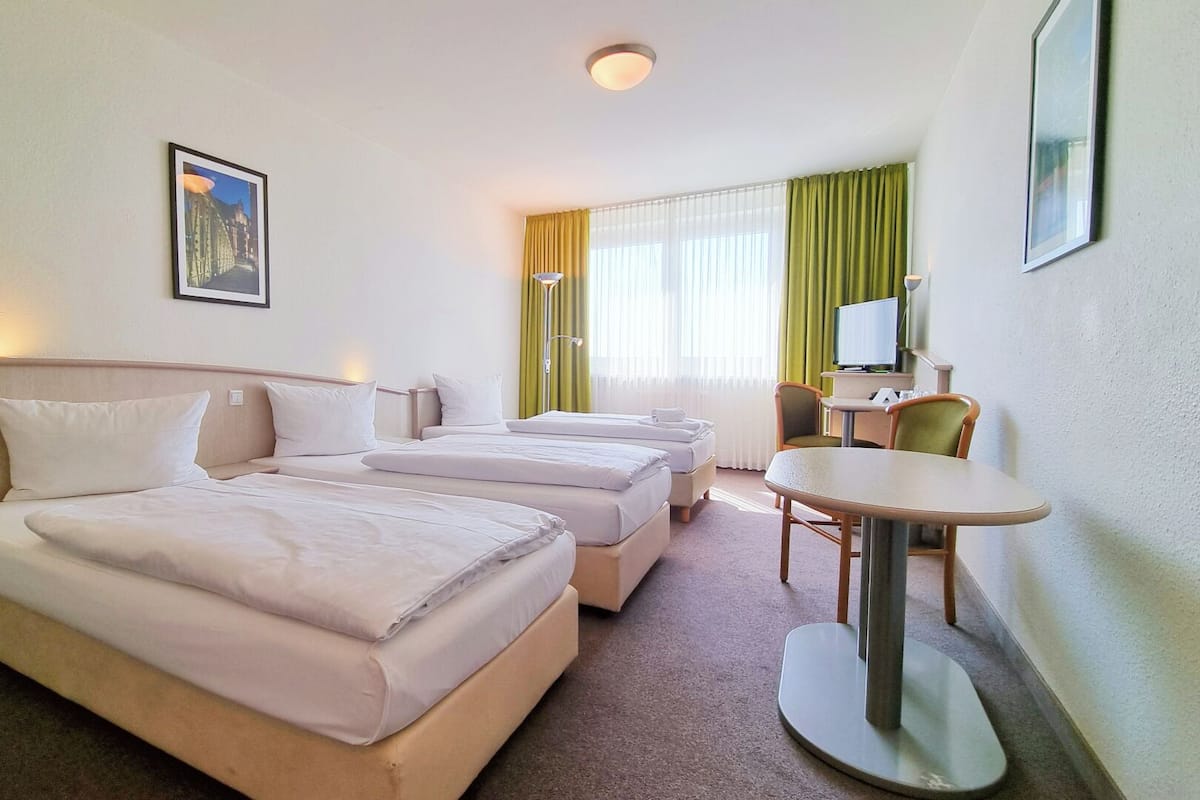 A hotel room with two beds, a small table, a chair, a TV, and a picture on the wall.
