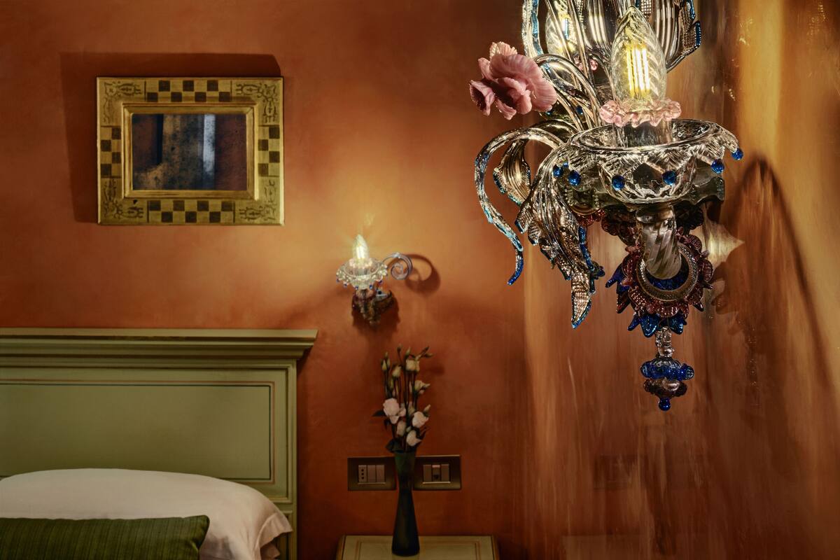 A room with a bed, a wall-mounted picture frame, a decorative wall sconce, and a chandelier.
