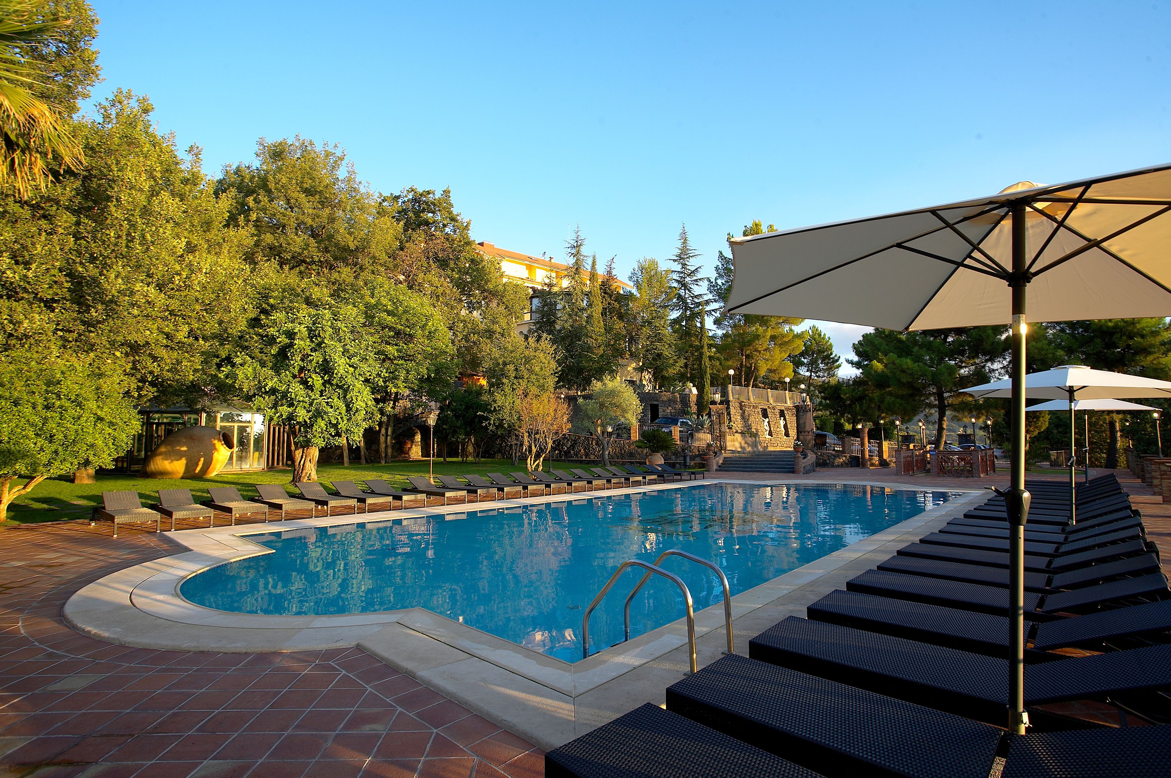 A swimming pool with lounge chairs and umbrellas, surrounded by trees and a stone building in the background.