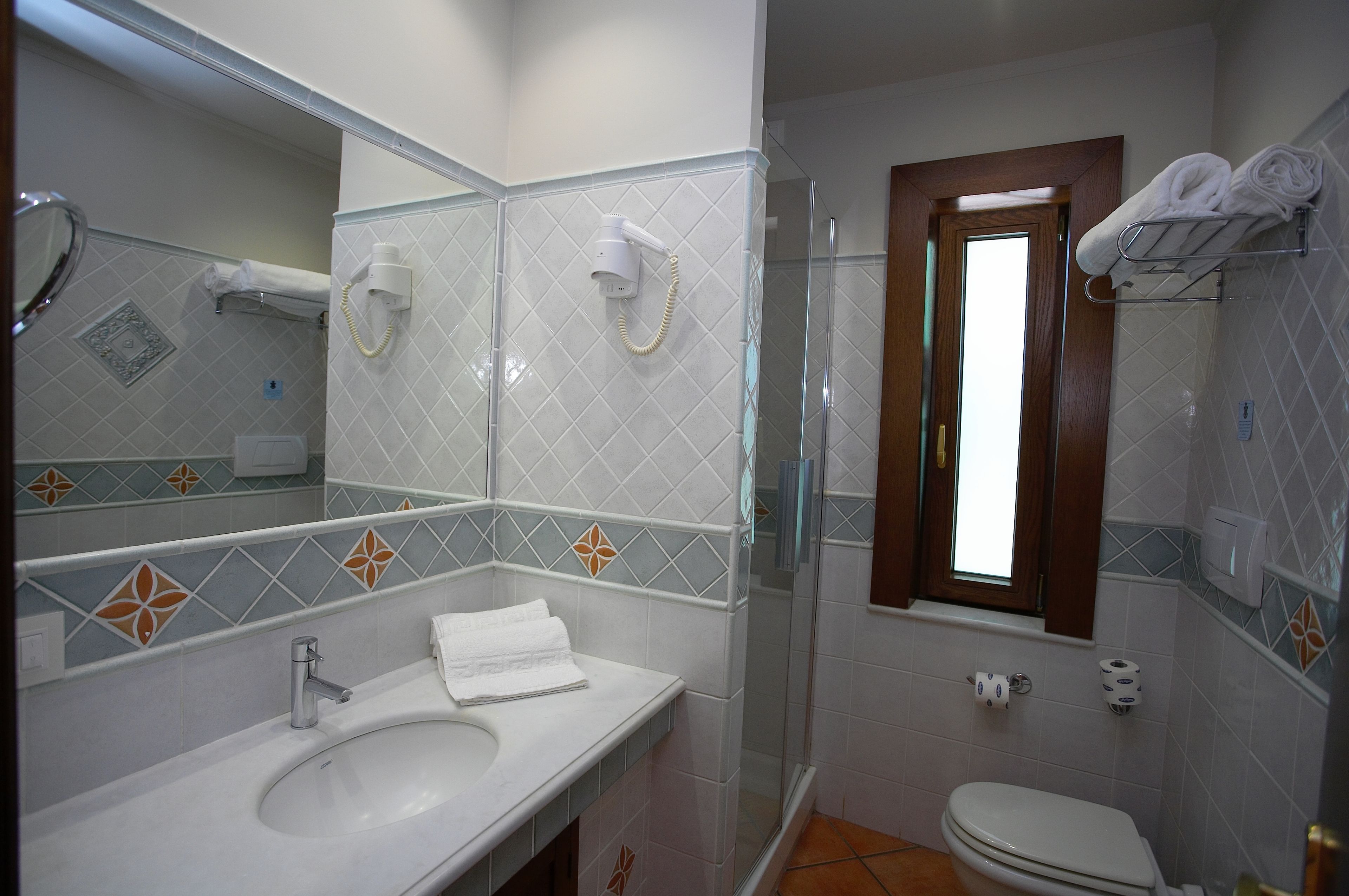 Une salle de bain comprenant un lavabo, un miroir, un porte-serviettes, une douche, des toilettes et une fenêtre.