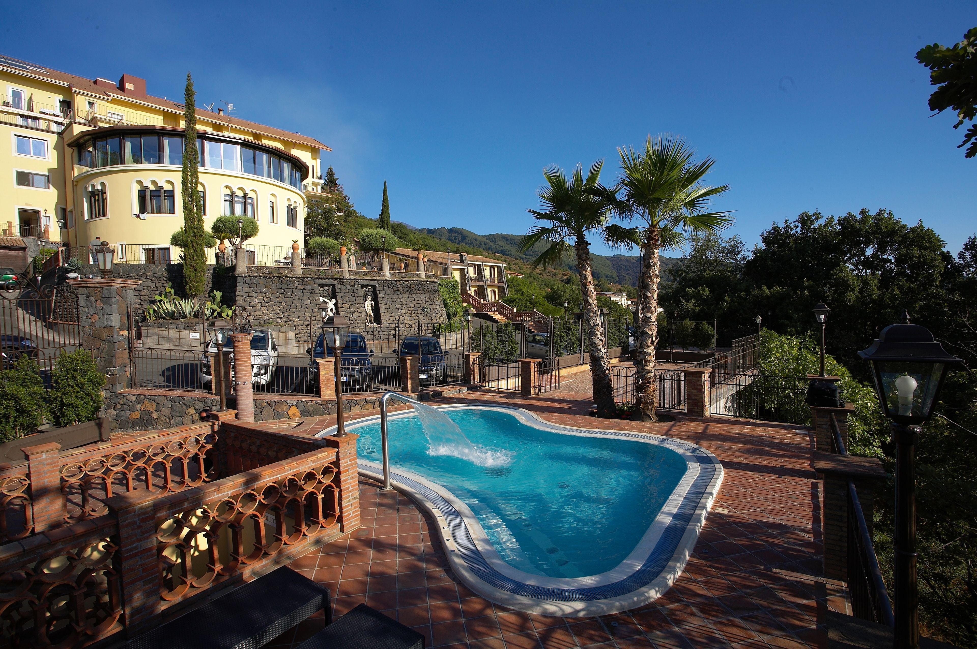 A swimming pool with a curved edge, surrounded by a stone wall and a metal railing.