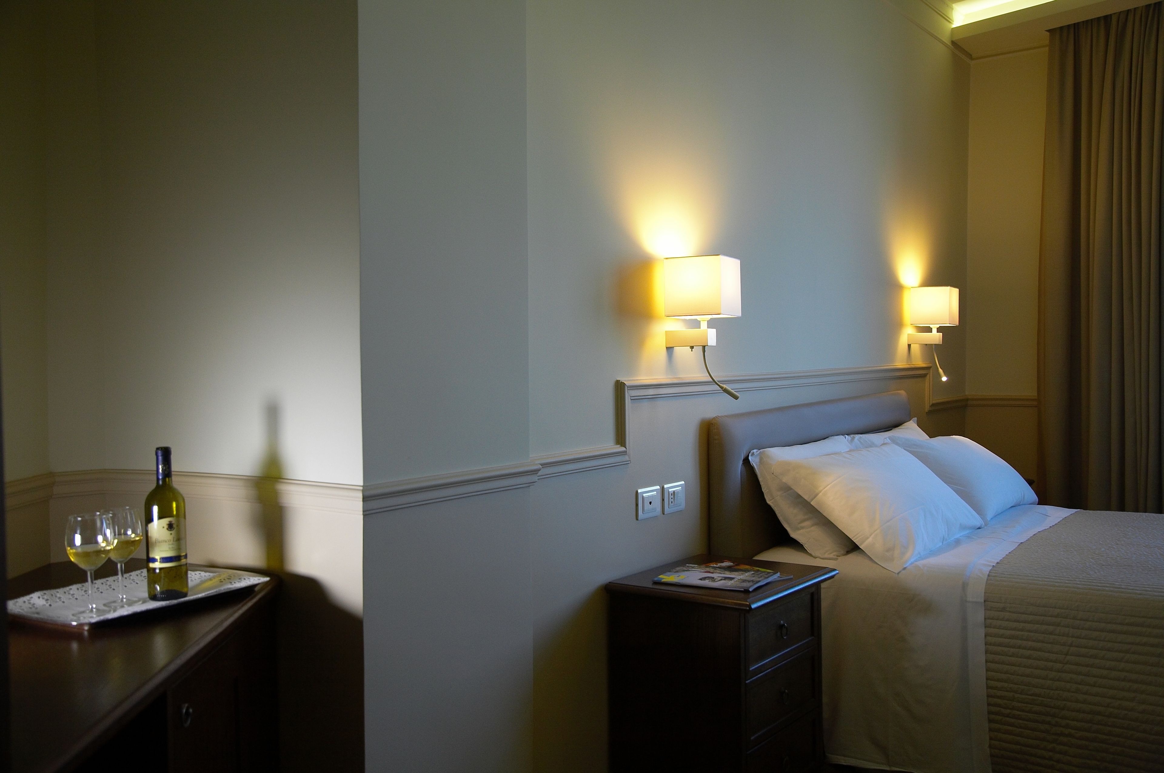 A hotel room with a bed, bedside tables, a nightstand, and two wall-mounted lamps.
