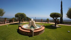 A circular fountain with a central water feature, surrounded by a well-maintained lawn and potted plants. - Airone Wellness Hotel (Zafferana Etnea)