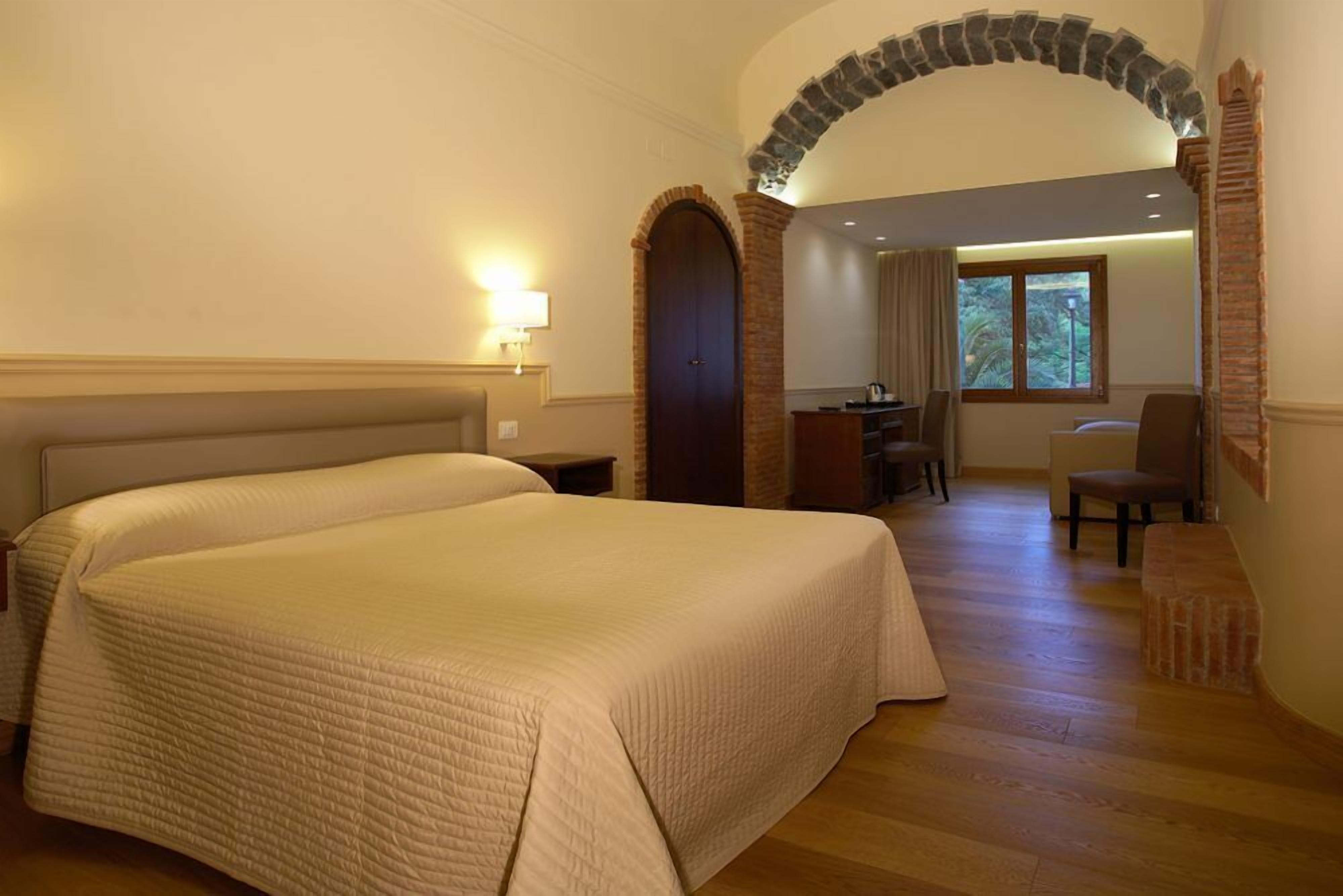 A hotel room with a large bed, a desk, and a chair.