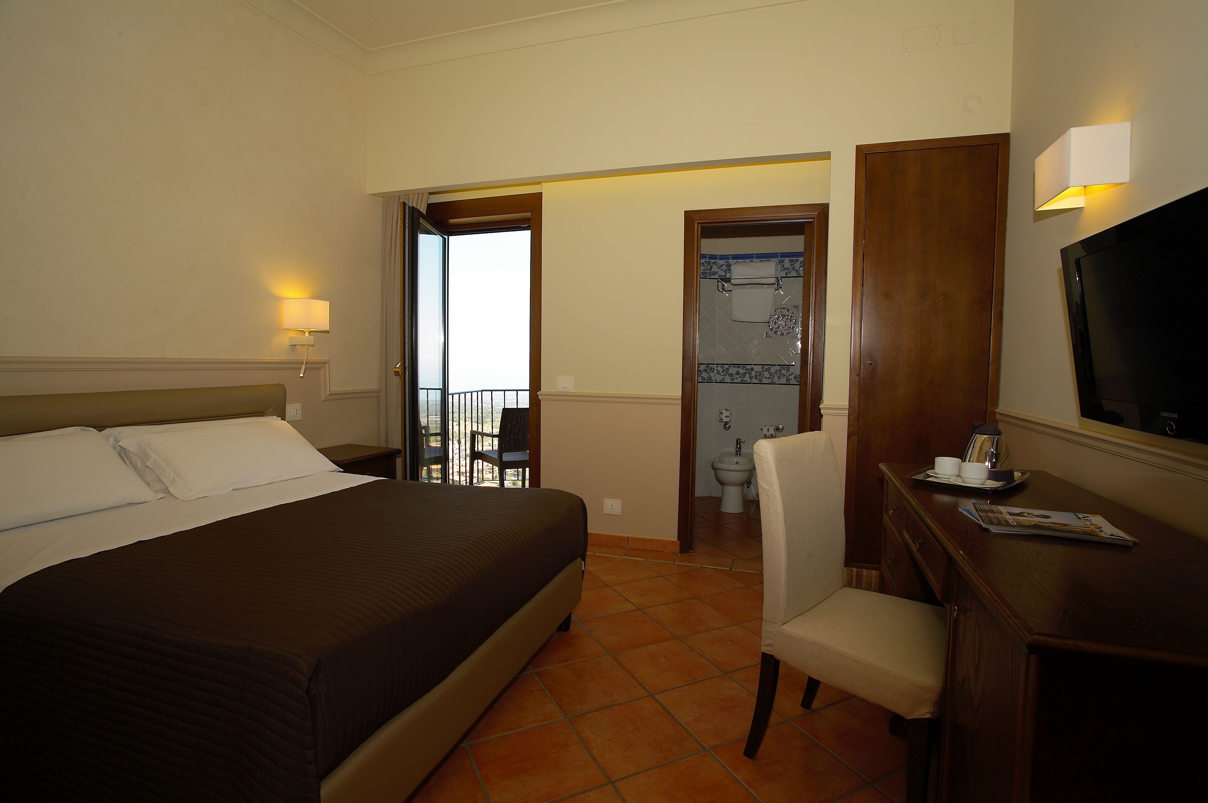 Habitación de hotel con una cama grande, un escritorio con silla, televisión y un baño visible a través de una puerta abierta.