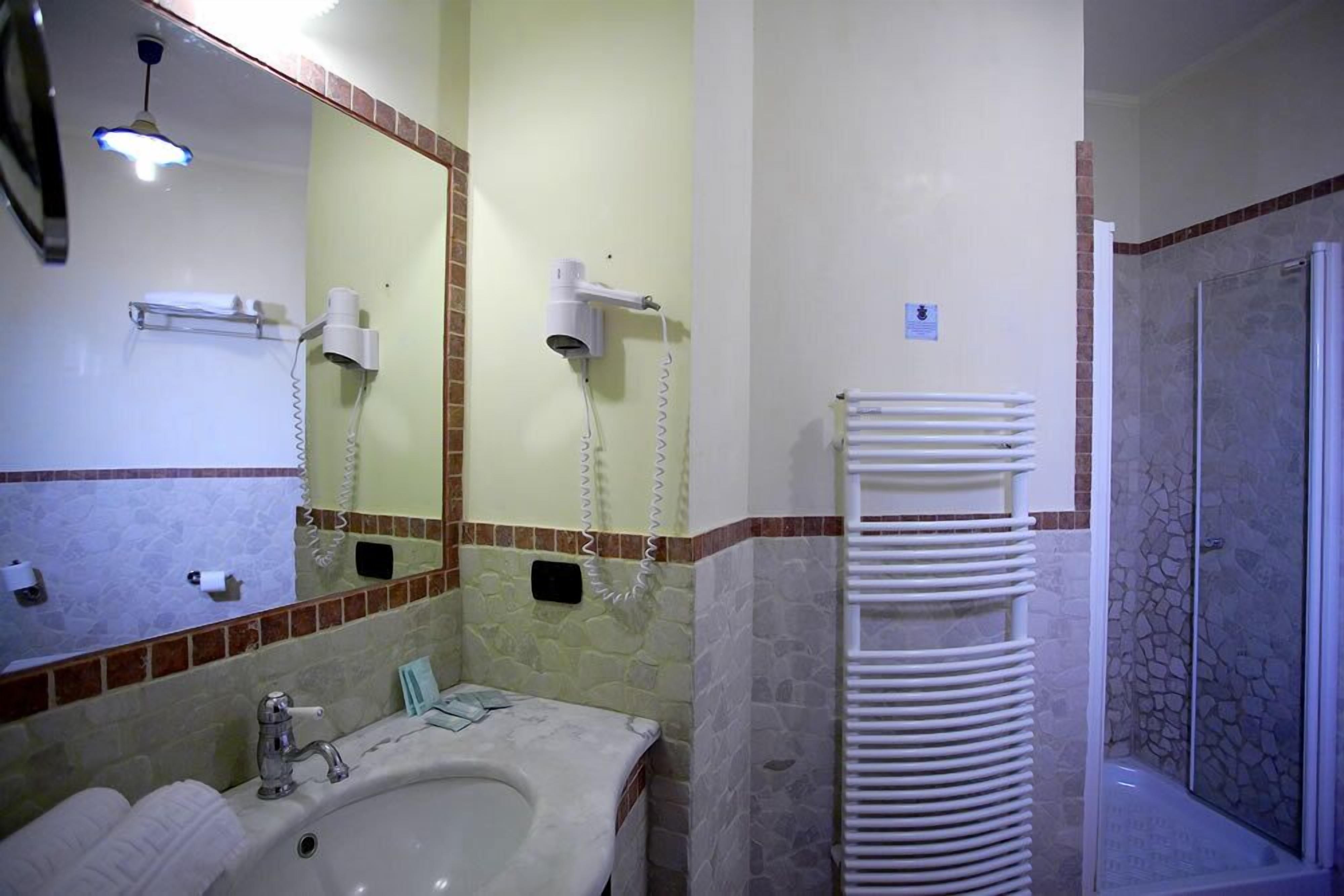 A bathroom with a sink, mirror, hairdryer, and a shower area.