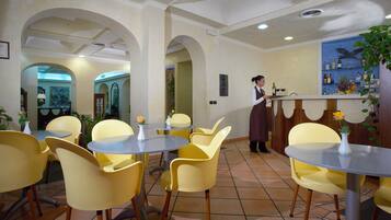 Interior de restaurante com cadeiras amarelas, mesas redondas e um espaço de bar.