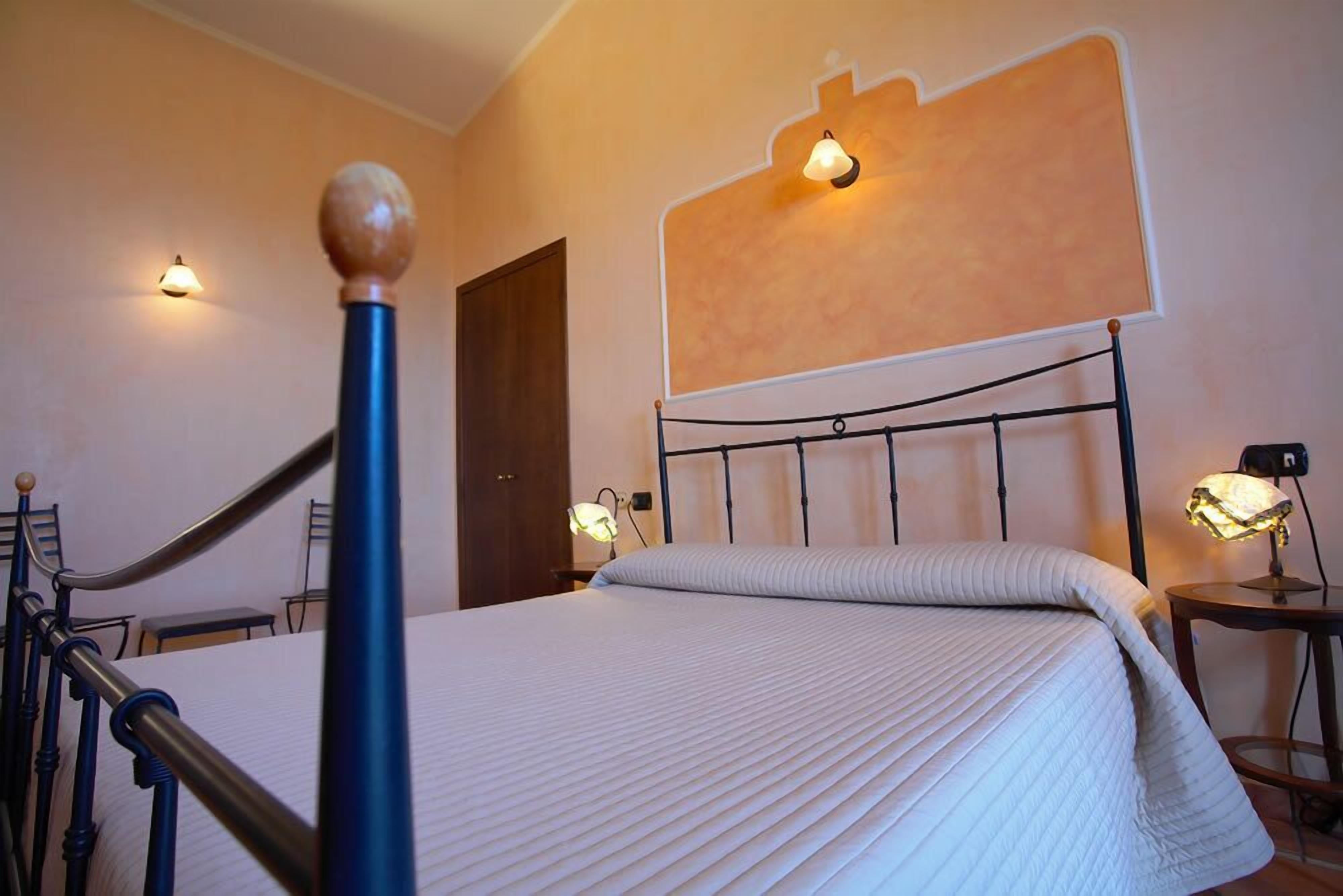 A bedroom with a bed, bedside lamps, a wooden door, and a wall-mounted light fixture.