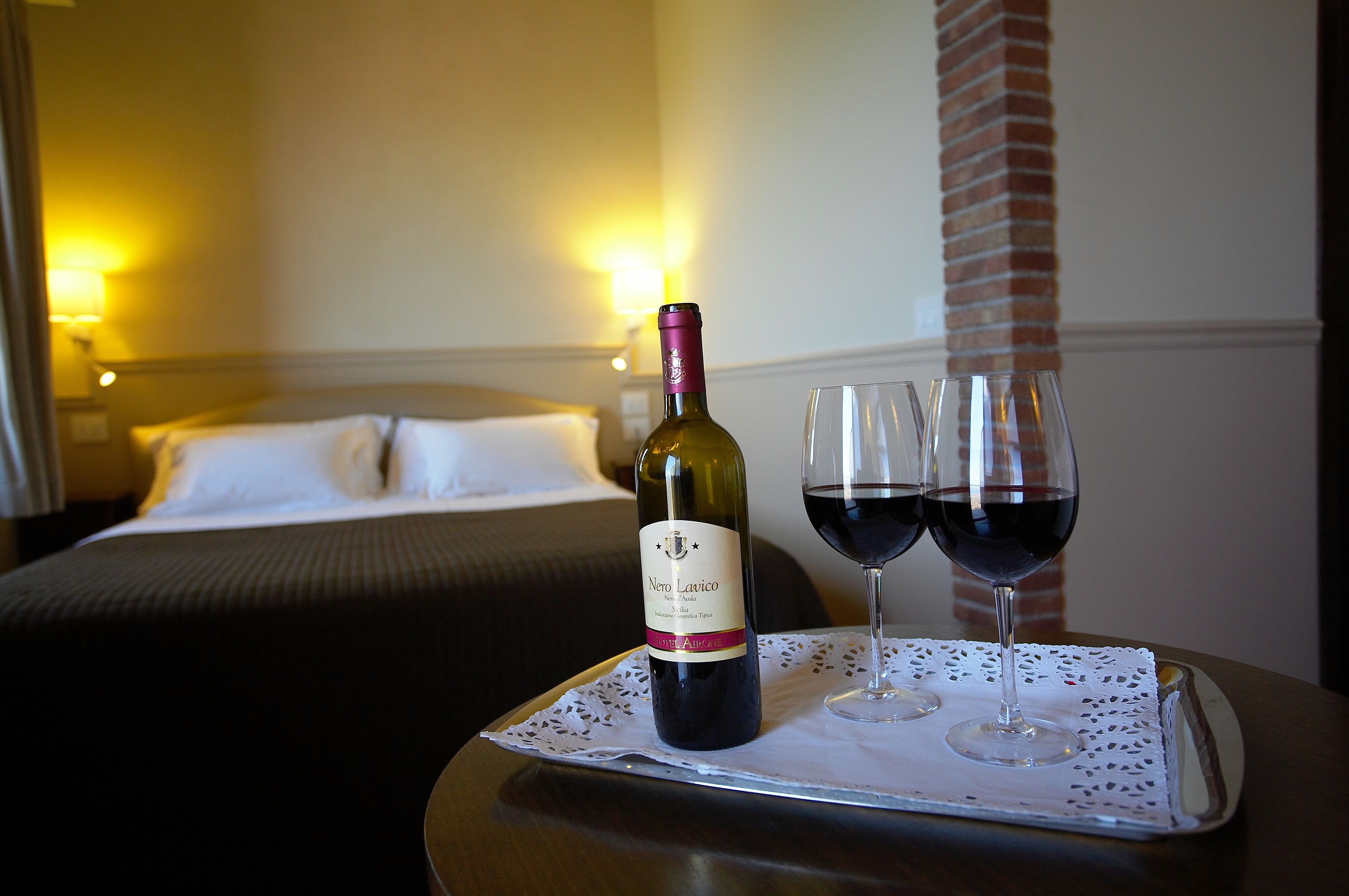 Habitación de hotel con una cama, una mesita de noche con una bandeja que contiene una botella de vino y dos copas.