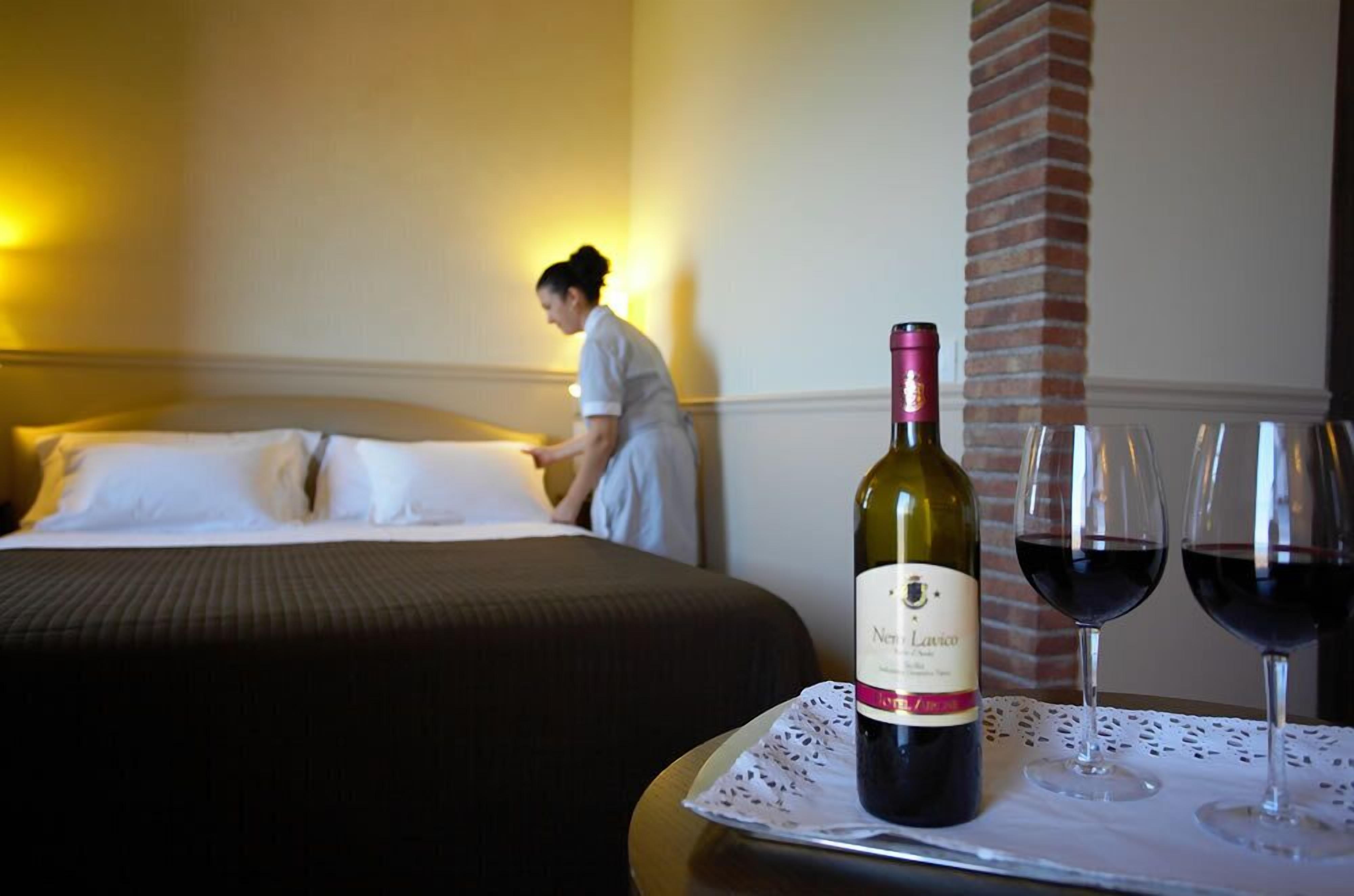 Una habitación de hotel con una cama bien hecha, una botella de vino y dos copas sobre una bandeja.