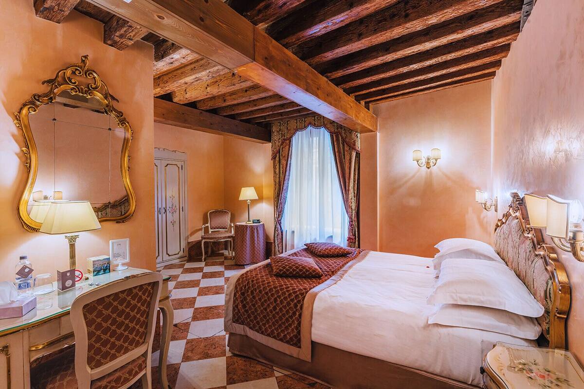 Habitación de hotel con piso a cuadros, cama con ropa de cama estampada, escritorio con lámpara, silla, espejo y armario.