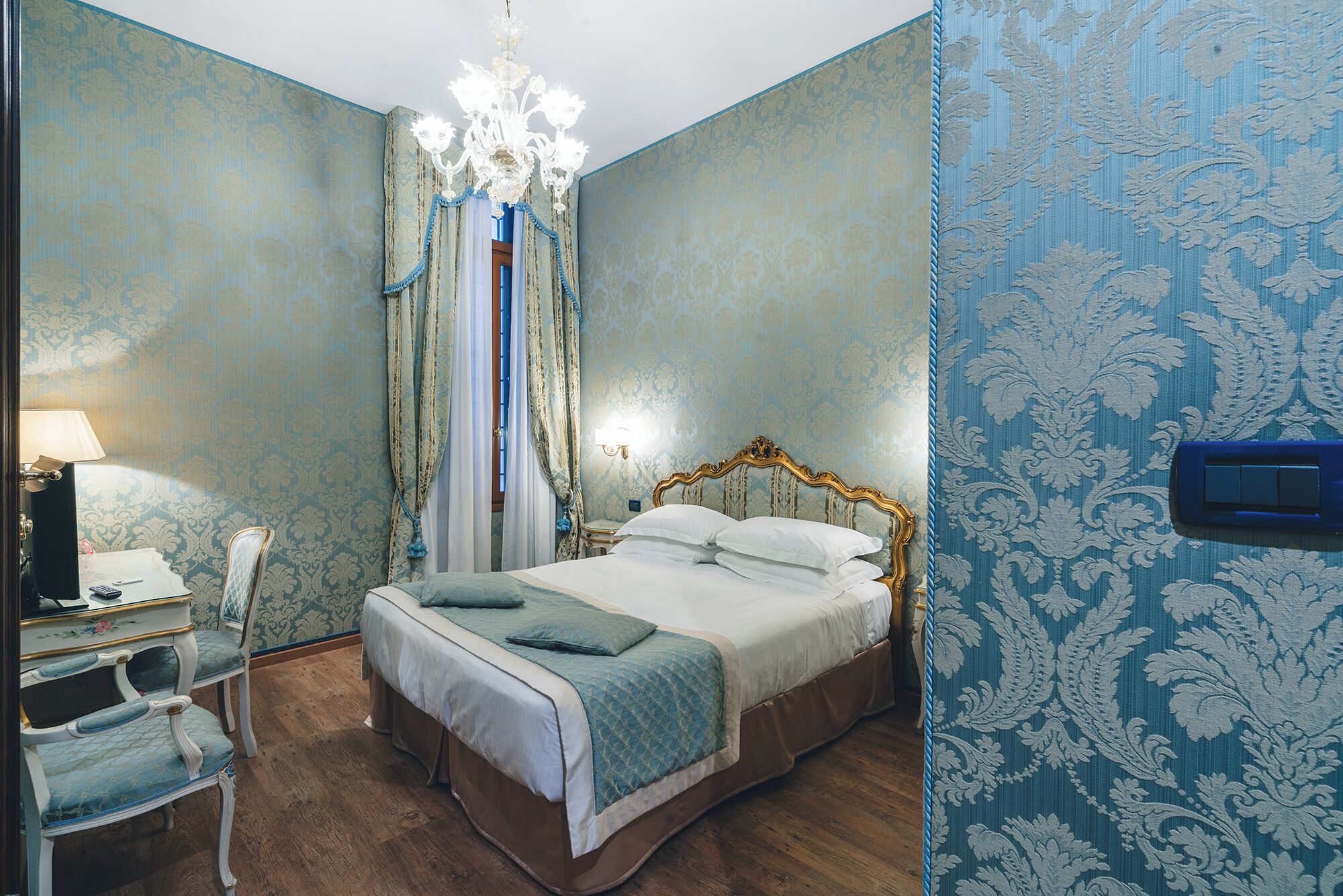A bedroom with a bed, a desk with a lamp, and a chair.