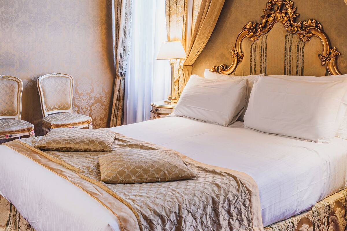 Una cama grande con cabecera decorada, dos mesitas de noche y un suelo cubierto de alfombra roja.