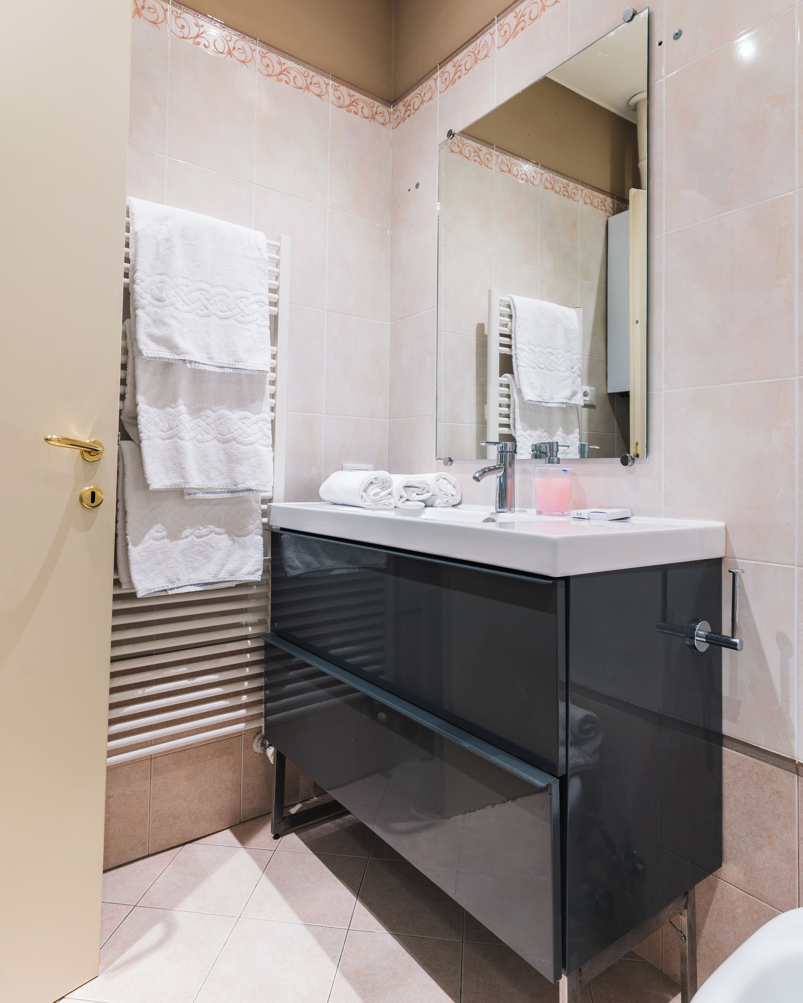 A modern bathroom with a glass-fronted vanity, a white sink, and a large mirror.