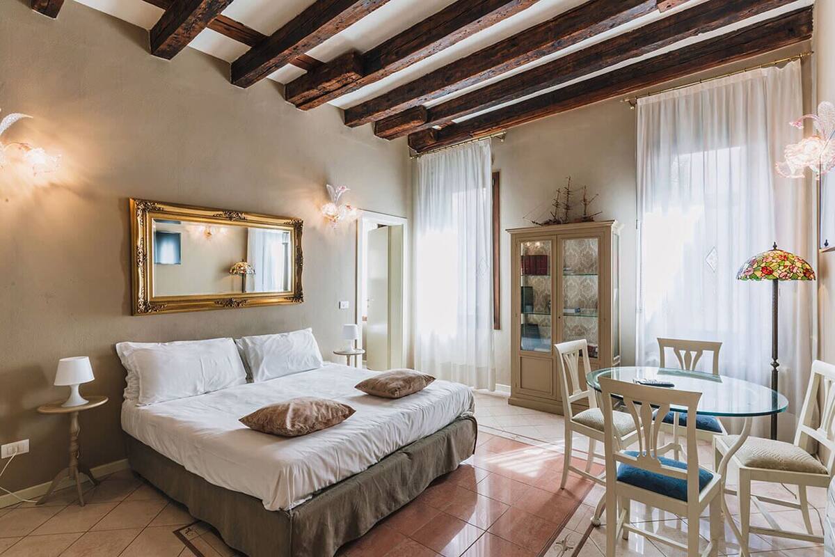 Un dormitorio con cama, una mesa redonda de vidrio con sillas, un armario y un espejo en la pared.