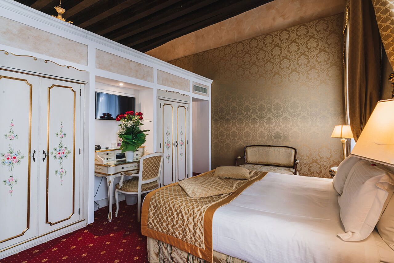 A hotel room with a bed, a desk with a chair, a wardrobe, and a TV.