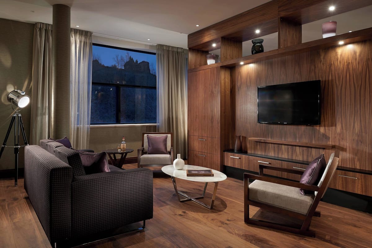 Un salon moderne avec un canapé, des fauteuils, une table basse et un téléviseur fixé au mur.